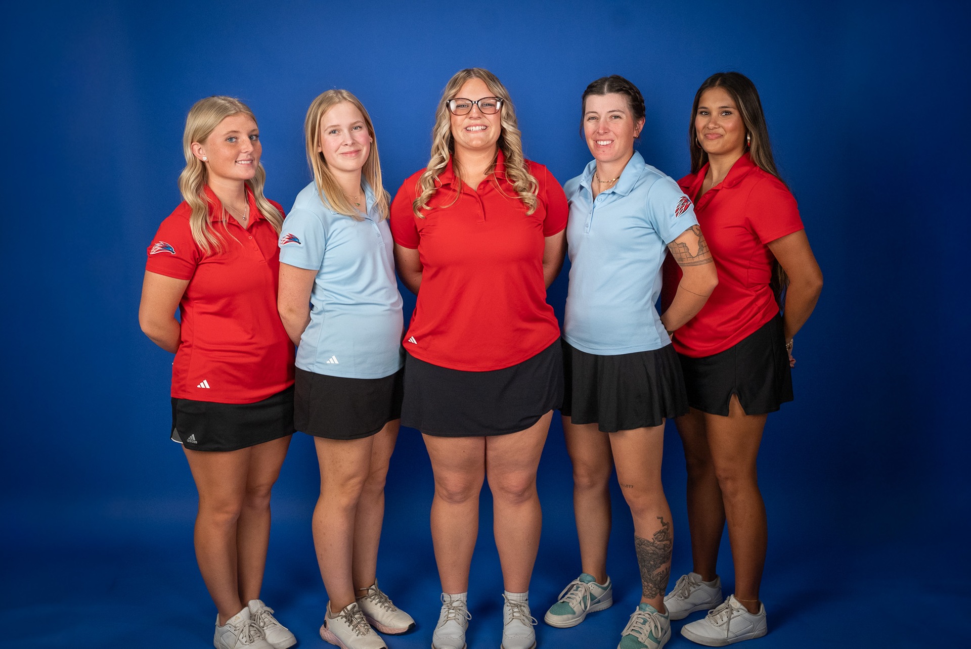 Photo: Five members of the Mesa Community College women&rsquo;s golf team pose together in front of a blue backdrop wearing team polos and black skirts. Three athletes wear red polos while two wear light blue polos, with all smiling for the team photo.
